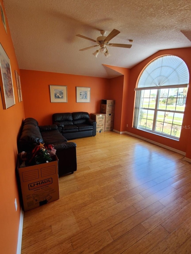 living room featuring a textured ceiling, ceiling fan, wood finished floors, and baseboards