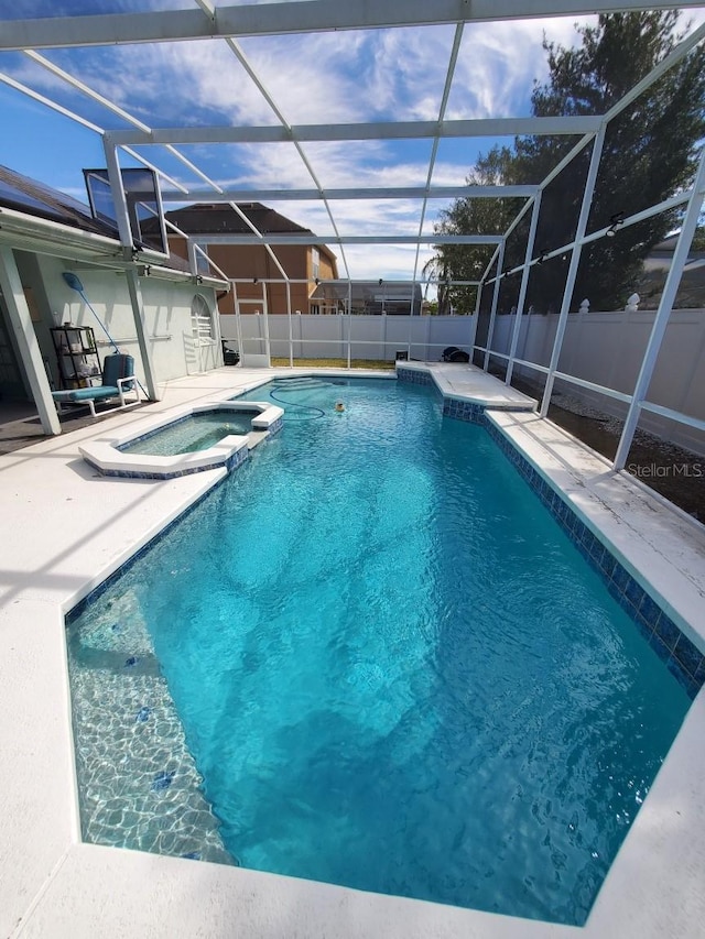 view of swimming pool featuring glass enclosure, a fenced backyard, a pool with connected hot tub, and a patio