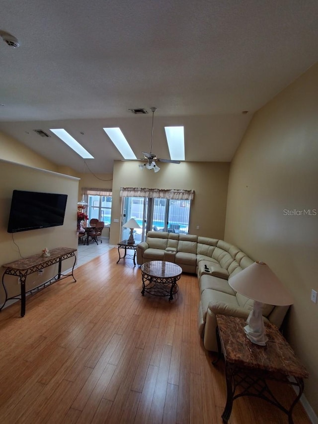 living room with vaulted ceiling with skylight, a textured ceiling, visible vents, and wood finished floors