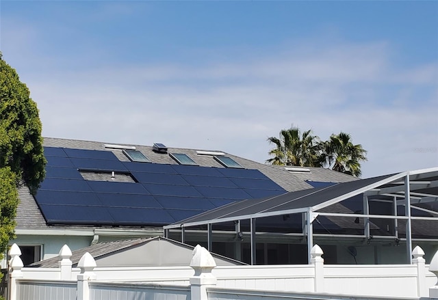 view of side of home featuring glass enclosure, solar panels, and roof with shingles