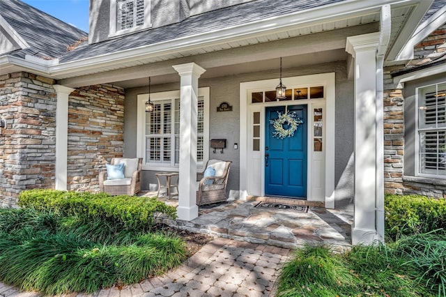 view of exterior entry featuring a porch, stone siding, and roof with shingles