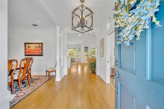 entryway featuring visible vents, an inviting chandelier, decorative columns, crown molding, and light wood-type flooring