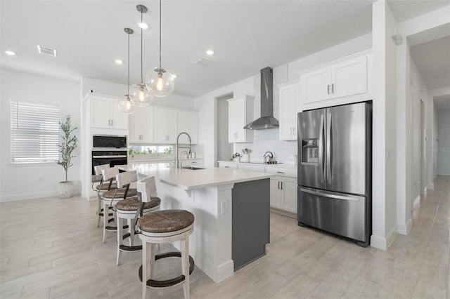 kitchen featuring wall chimney range hood, a center island with sink, a breakfast bar, light countertops, and stainless steel appliances