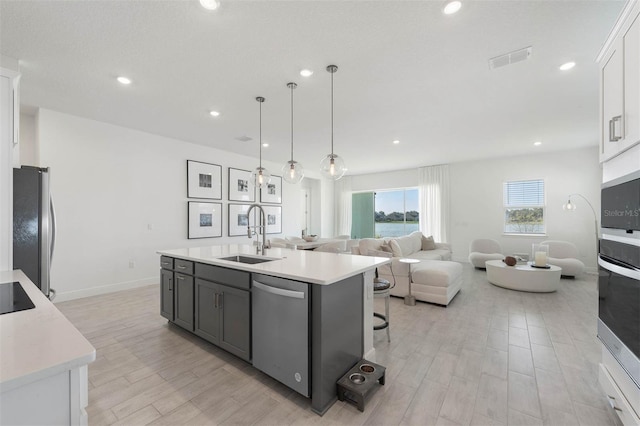 kitchen featuring visible vents, stainless steel appliances, a sink, light countertops, and open floor plan