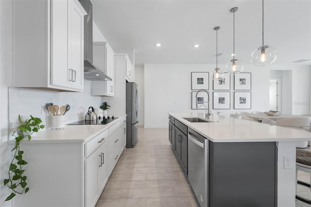 kitchen with light countertops, wall chimney range hood, an island with sink, and appliances with stainless steel finishes