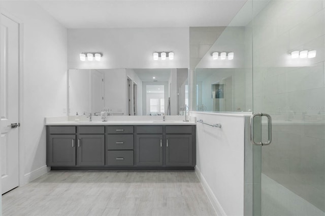 full bath featuring a sink, a stall shower, baseboards, and double vanity