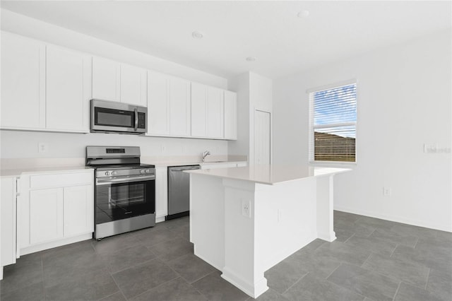 kitchen with light countertops, appliances with stainless steel finishes, white cabinetry, a kitchen island, and a sink