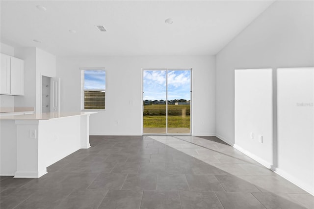 unfurnished living room featuring tile patterned flooring, visible vents, vaulted ceiling, and baseboards