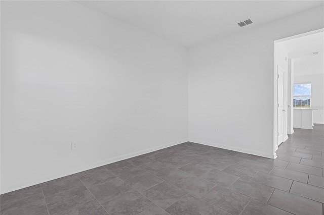 empty room featuring dark tile patterned floors, baseboards, and visible vents