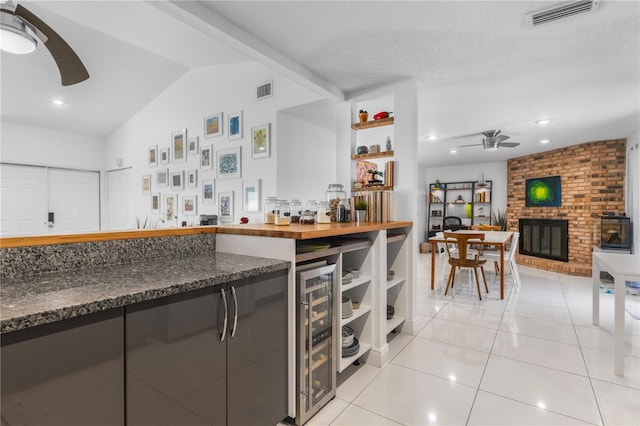 kitchen featuring visible vents, ceiling fan, wine cooler, vaulted ceiling, and a fireplace