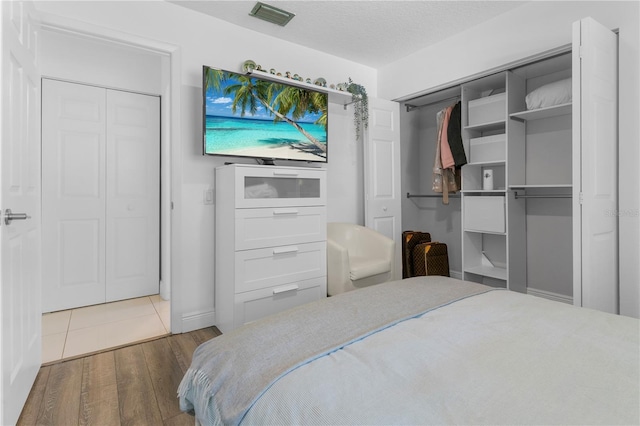 bedroom with a closet, a textured ceiling, visible vents, and wood finished floors