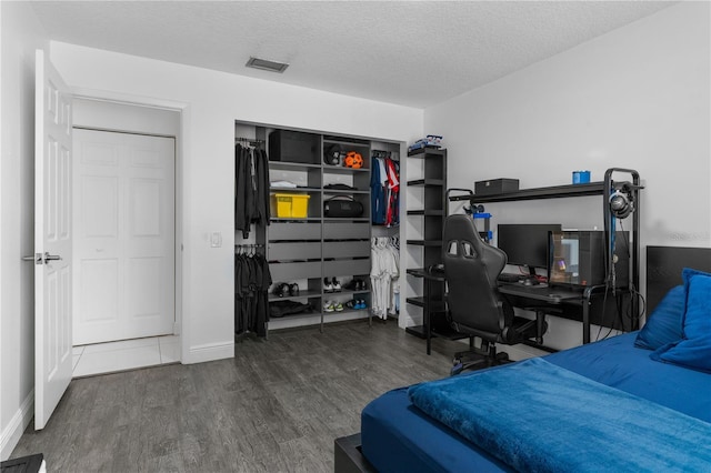 bedroom featuring baseboards, a textured ceiling, visible vents, and wood finished floors