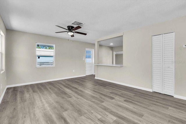 empty room with a ceiling fan, wood finished floors, visible vents, and baseboards