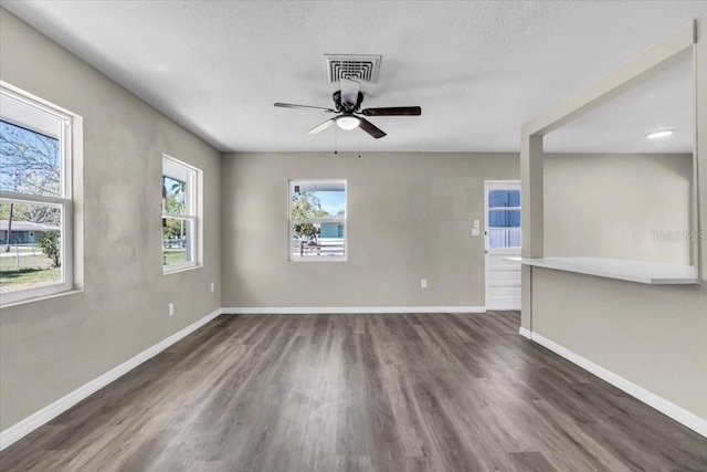 empty room with baseboards, visible vents, ceiling fan, dark wood-style flooring, and a textured ceiling