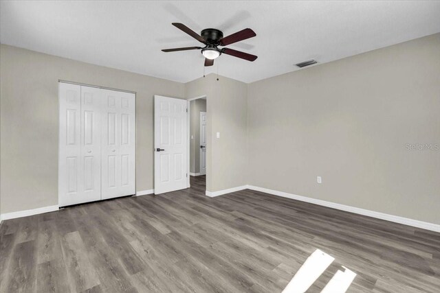 unfurnished bedroom with a closet, wood finished floors, visible vents, and baseboards