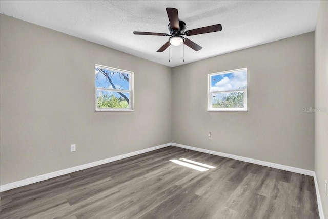 empty room with a wealth of natural light, a textured ceiling, baseboards, and wood finished floors