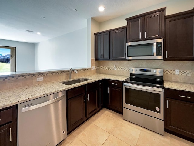 kitchen with a sink, backsplash, stainless steel appliances, dark brown cabinetry, and light stone countertops