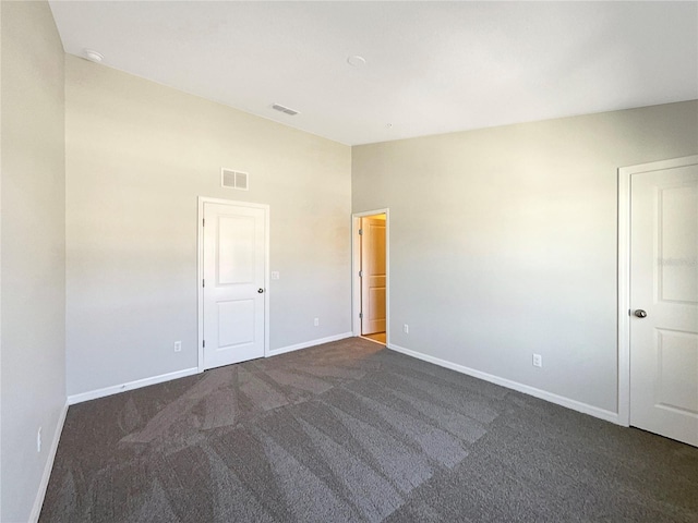 unfurnished bedroom featuring dark colored carpet, visible vents, baseboards, and lofted ceiling