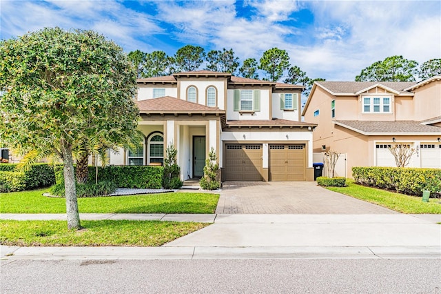 mediterranean / spanish house with decorative driveway, an attached garage, a front yard, and stucco siding