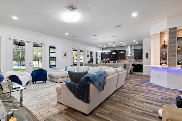 living room featuring a textured ceiling, recessed lighting, wood finished floors, visible vents, and french doors