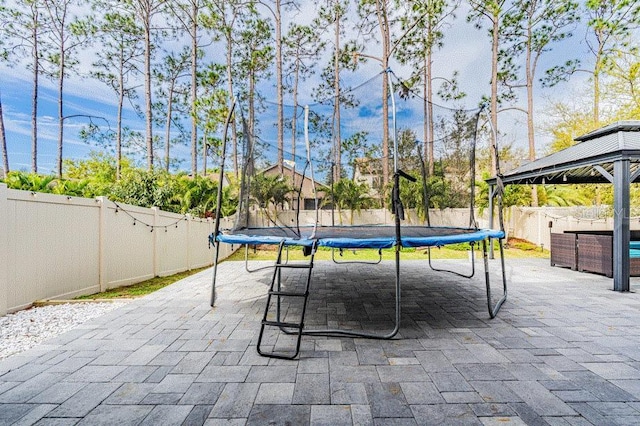 view of patio featuring a trampoline, a fenced backyard, and a gazebo