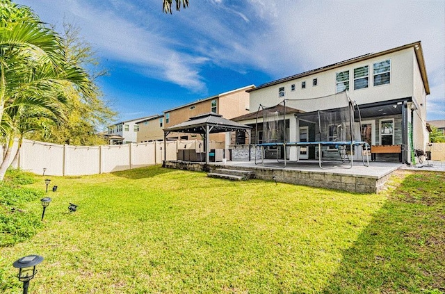 back of house featuring a yard, a trampoline, a gazebo, and fence