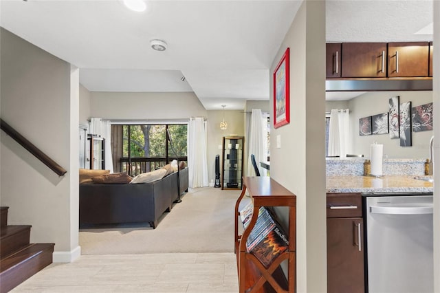 kitchen featuring light stone counters, open floor plan, dark brown cabinetry, dishwasher, and baseboards