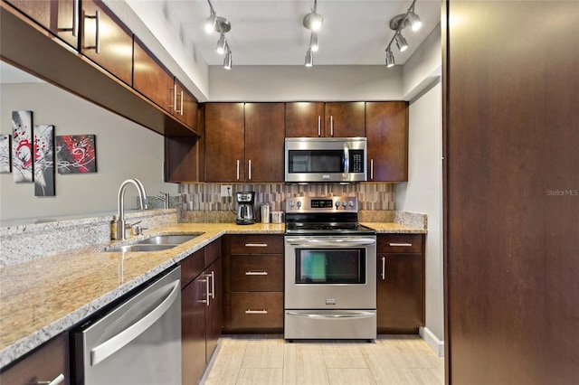 kitchen with light stone counters, dark brown cabinetry, stainless steel appliances, a sink, and backsplash