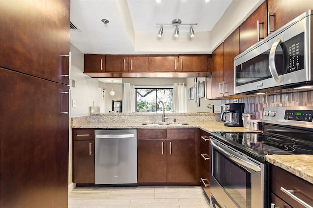 kitchen with light tile patterned floors, light stone counters, stainless steel appliances, a sink, and decorative backsplash