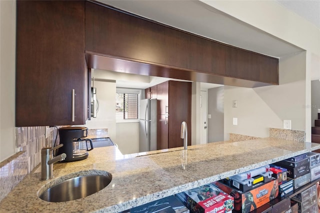 kitchen with a peninsula, light stone countertops, appliances with stainless steel finishes, and a sink