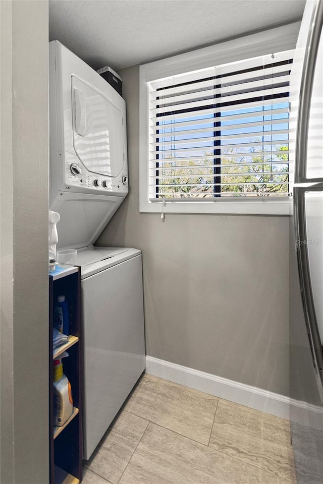 laundry room featuring a textured ceiling, laundry area, stacked washer and clothes dryer, and baseboards