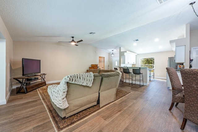 living area featuring visible vents, baseboards, lofted ceiling, wood finished floors, and a textured ceiling