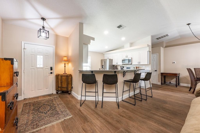 kitchen with visible vents, a kitchen breakfast bar, stainless steel appliances, white cabinets, and vaulted ceiling