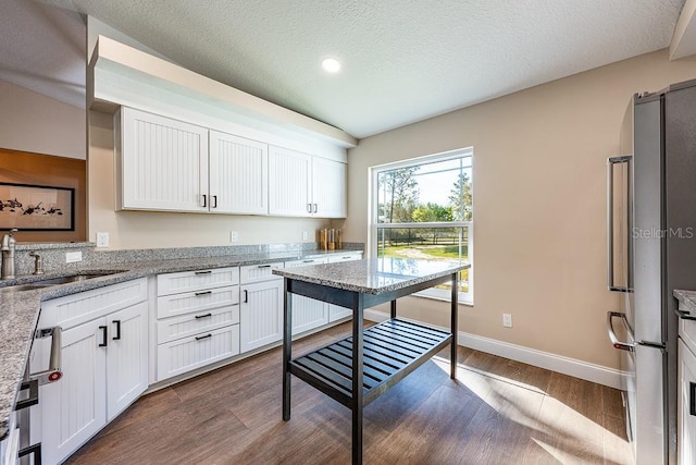 kitchen featuring white cabinets, light stone countertops, dark wood-style flooring, and a sink