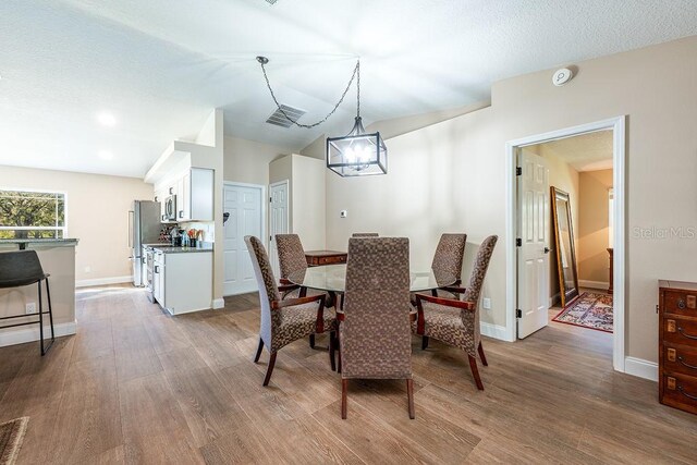 dining area featuring visible vents, baseboards, a textured ceiling, and wood finished floors