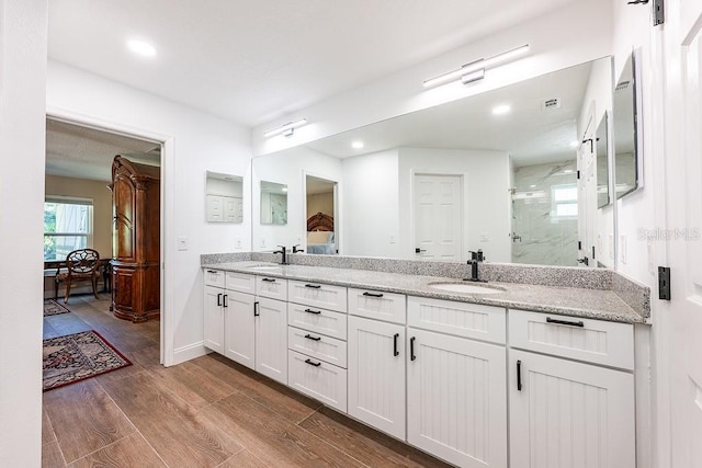 bathroom with a sink, a marble finish shower, wood finished floors, and double vanity