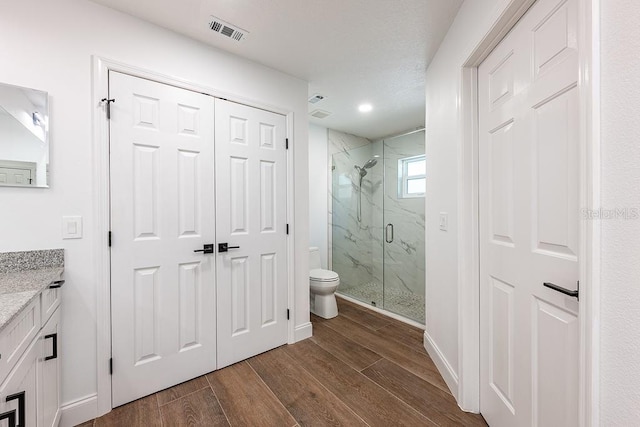 full bath with a marble finish shower, visible vents, wood tiled floor, toilet, and vanity