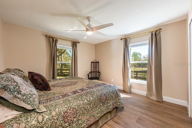 bedroom with a ceiling fan, wood finished floors, baseboards, and a textured ceiling