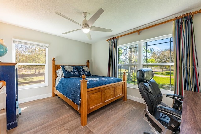 bedroom featuring a ceiling fan, wood finished floors, baseboards, and a textured ceiling