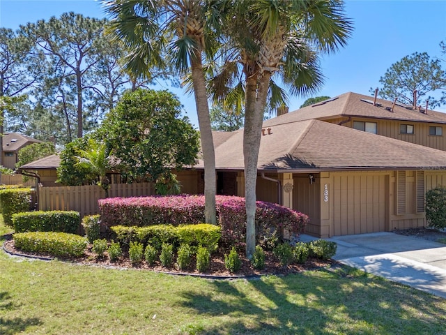 view of front of home featuring roof with shingles, concrete driveway, a front lawn, and fence