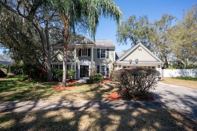 colonial-style house featuring concrete driveway, an attached garage, fence, and a front yard