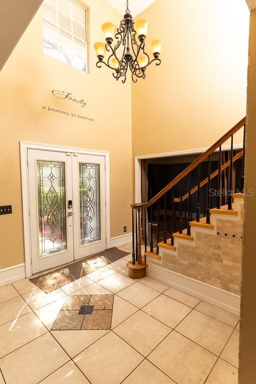 tiled foyer with a towering ceiling, french doors, baseboards, a chandelier, and stairs