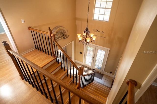 stairway featuring wood finished floors, baseboards, a high ceiling, french doors, and a notable chandelier