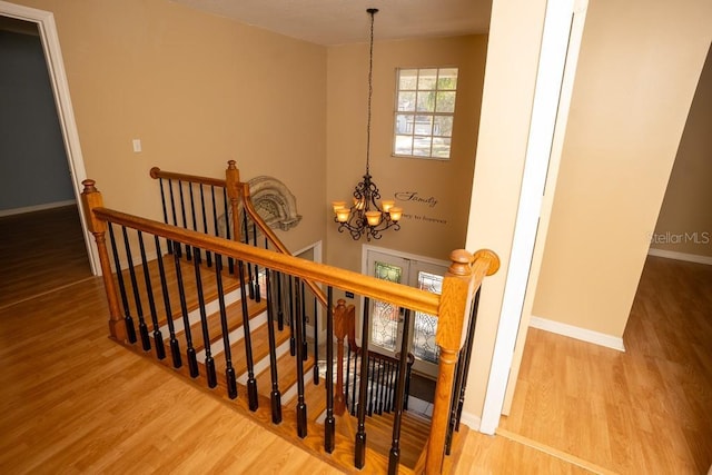 staircase with a notable chandelier, baseboards, and wood finished floors