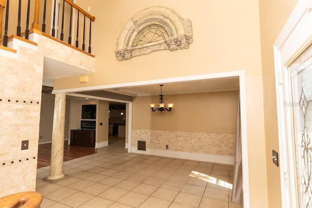 entrance foyer featuring visible vents, a chandelier, a towering ceiling, tile patterned floors, and ornate columns