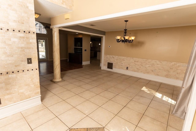 spare room featuring baseboards, ornamental molding, light tile patterned floors, an inviting chandelier, and ornate columns