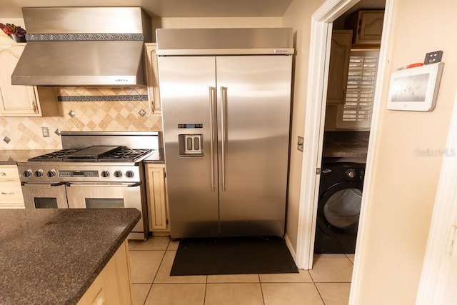 kitchen featuring decorative backsplash, high end appliances, light tile patterned flooring, washer / clothes dryer, and wall chimney exhaust hood