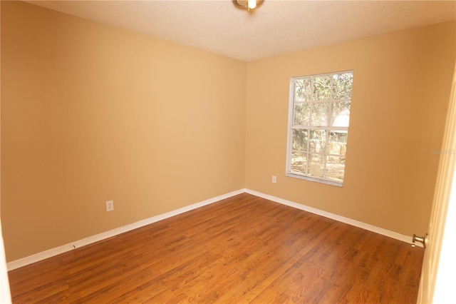 unfurnished room featuring a textured ceiling, baseboards, and wood finished floors