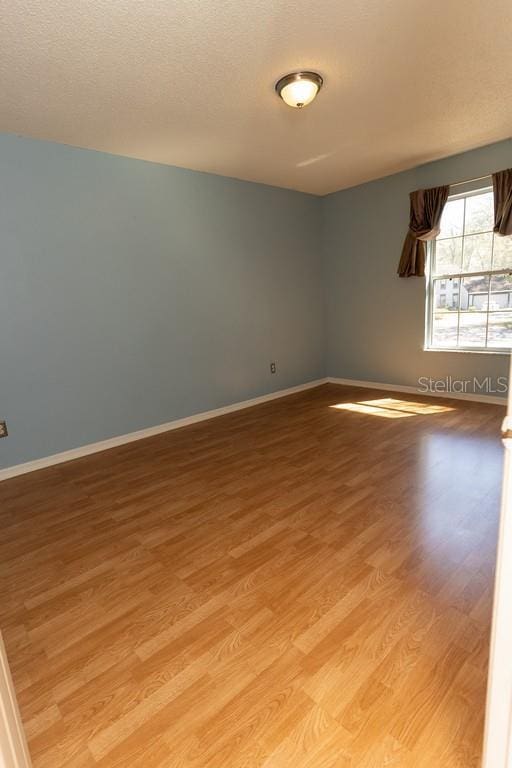 empty room with a textured ceiling, baseboards, and light wood-style floors