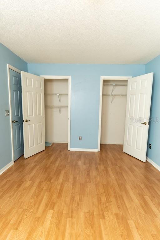 unfurnished bedroom featuring a textured ceiling, two closets, light wood-type flooring, and baseboards